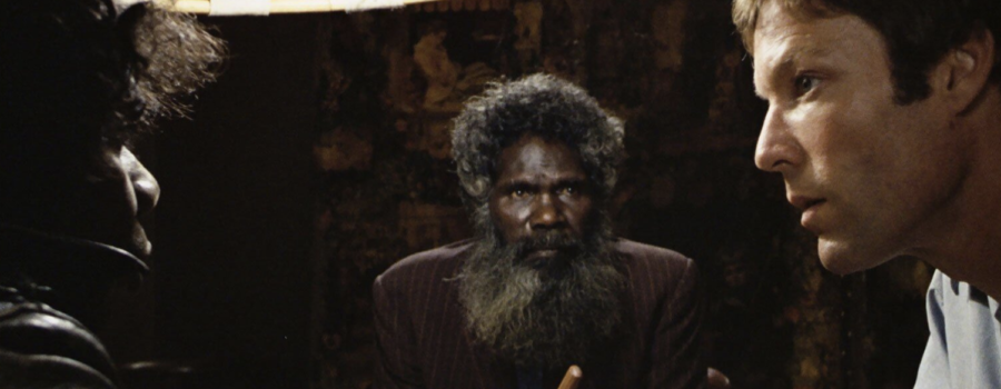 Three men sit around a table. The one on the left and the middle are Aboriginal men, the one on the right is a white lawyer.