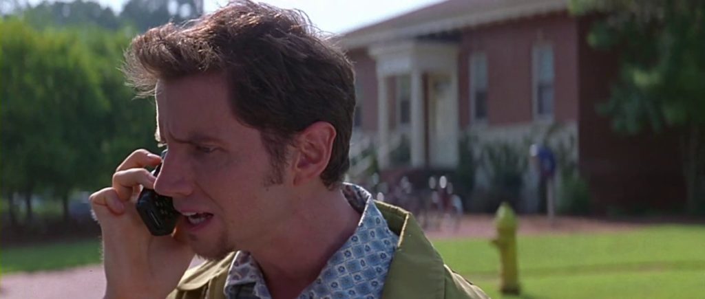 Jamie Kennedy as Randy Meeks, standing to the left of a red brick building. He is wearing a blue floral buttondown under a green jacket. He is facing the left, speaking on a flip phone.