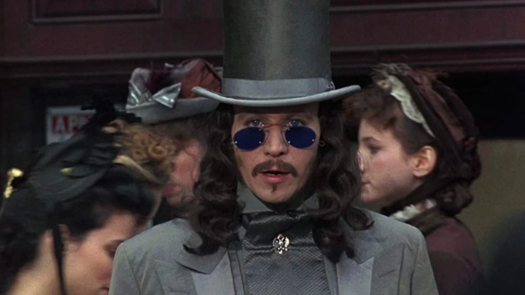 A youthful Dracula in gray suit and top hat with blue sunglasses stares open-mouthed as crowds pass around him