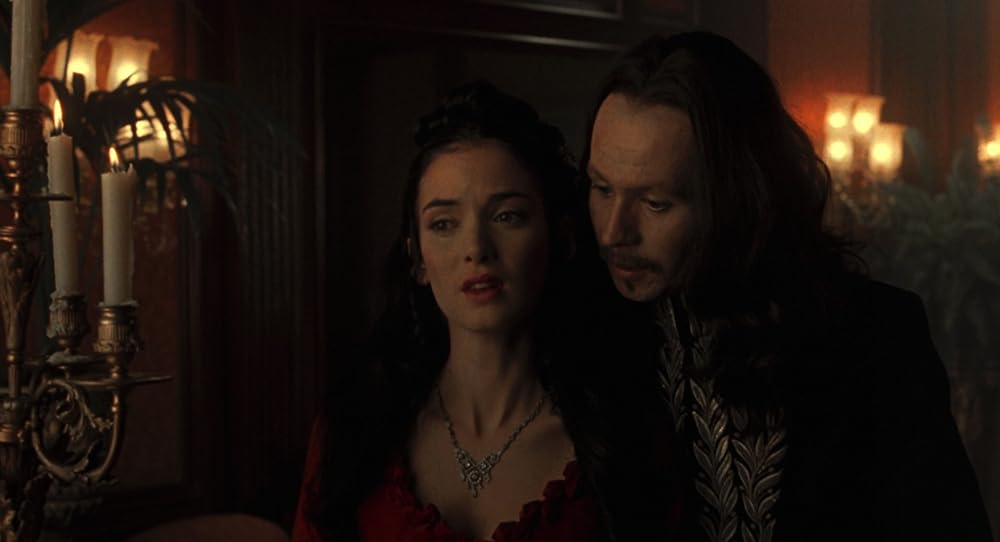 Gary Oldman as Dracula, a white adult man with long brown hair and a goatee, stands close to Winona Ryder as Mina Harker, whispering in her ear