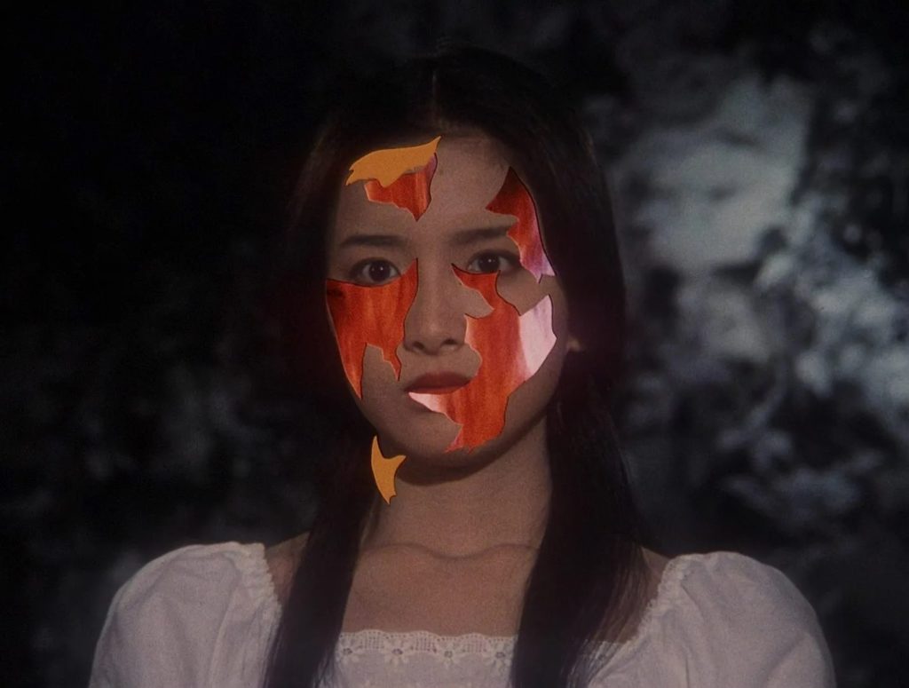 A young Asian woman in a white dress with shards of her face falling away to reveal a superimposed image of fire.