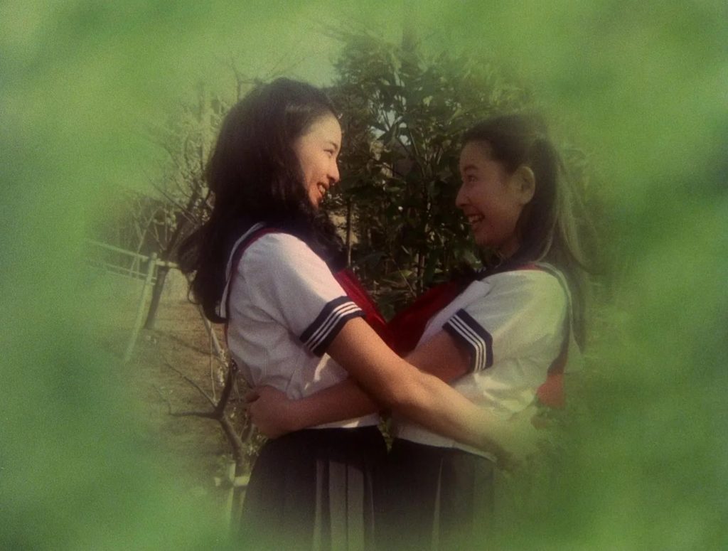 Two young Asian women in school uniforms smiling at each other and embracing, surrounded by a green vignette tint.