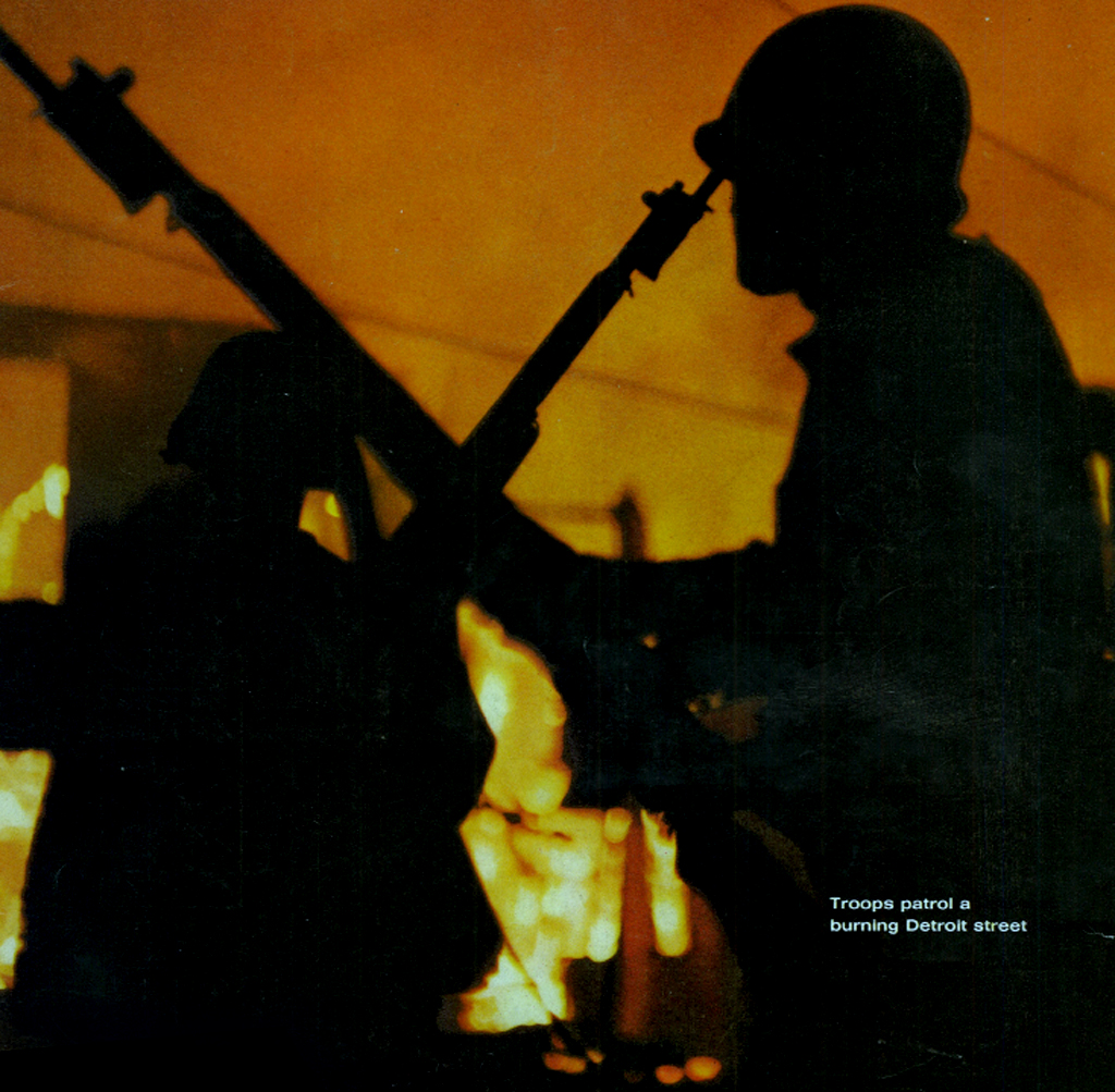 2 American soldiers holding machine gun rifles walk over a fiery hill by night