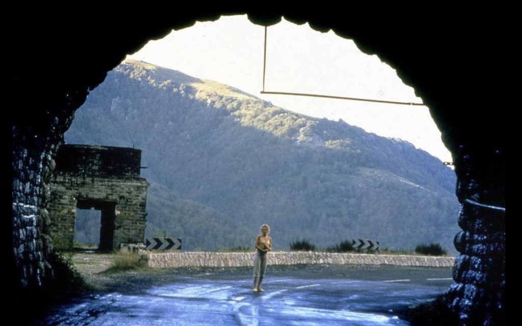 Saskia stands outside of a highway tunnel with a green mountain in the distance