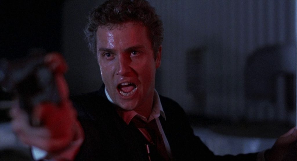 William Petersen as Agent Richard Chance points a gun at someone off-screen; he is yelling.