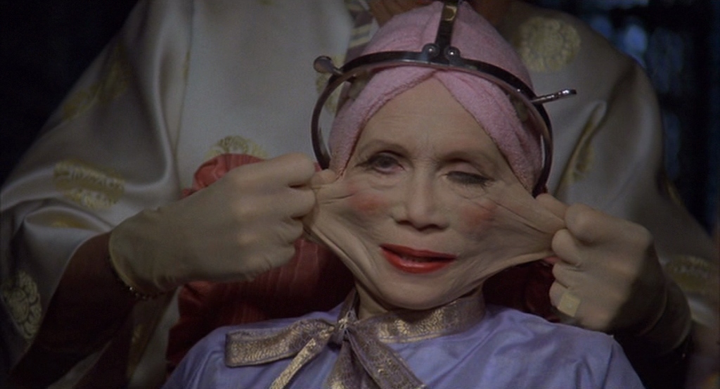 Ida Lowry (Katherine Helmond) has her face stretched to grotesque extremes by her plastic surgeon (Jim Broadbent).