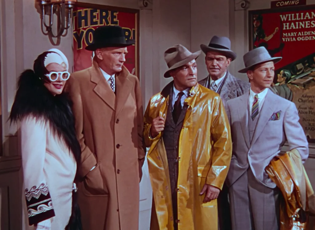 A still from Singin’ in the Rain depicting the moment after the characters sat in on a screening of The Dueling Cavalier, looking disappointed and concerned in the theater lobby towards the camera.