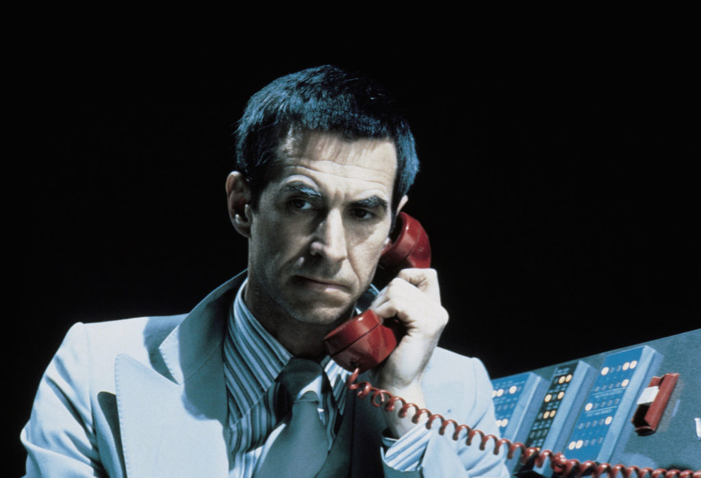 Anthony Perkins suspiciously holds a red telephone reciever to his ear, from the film Winter Kills. 