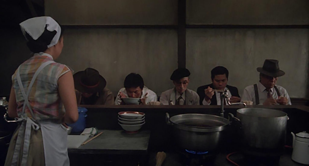 Tampopo is behind the counter in her kitchen, waiting to hear feedback from her mentors about her improved ramen recipe. 