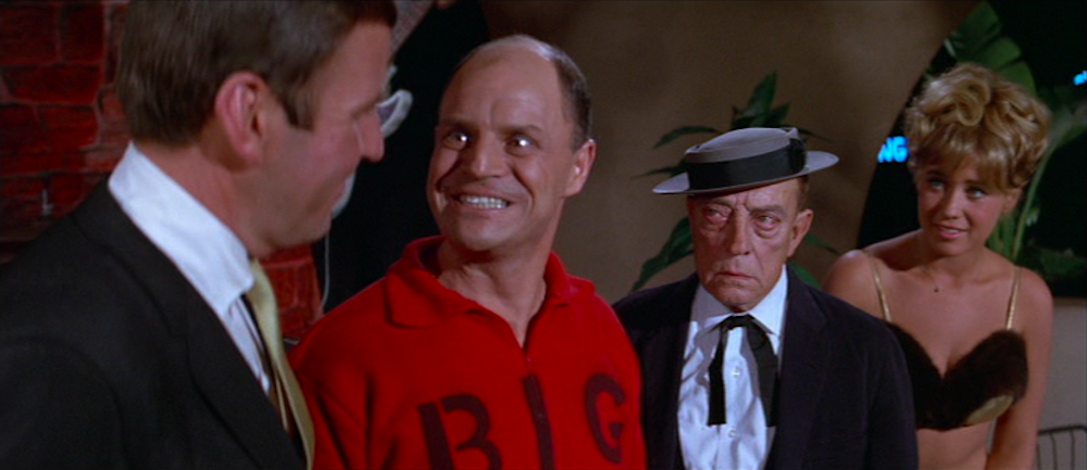 a balding white man grinning maniacally at another man with his back to the camera; behind these two are an elderly white man and white blonde woman in a bikini
Image sourced from Fallen Rocket.