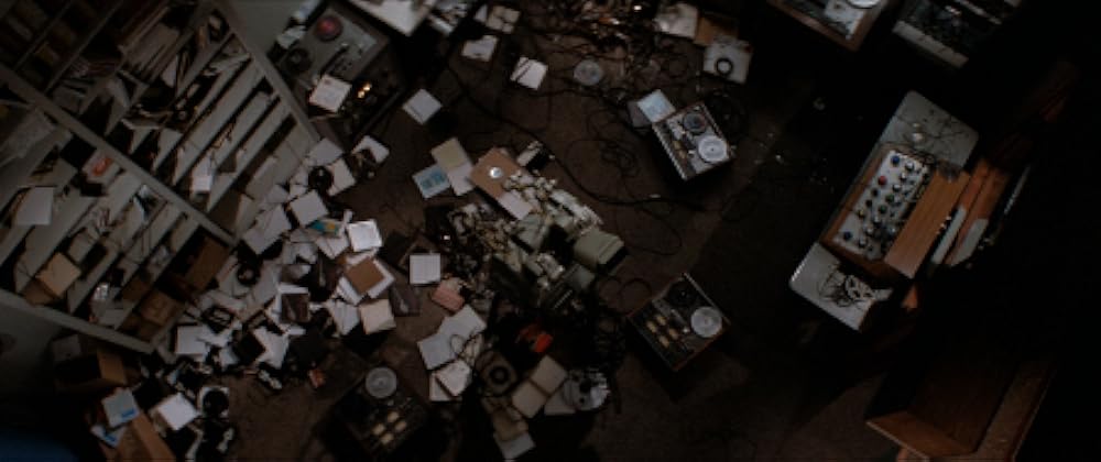 A birds-eye shot of a room filled with sound equipment, with tape recorders, players, cables, and cases of tape scattered on all surfaces.