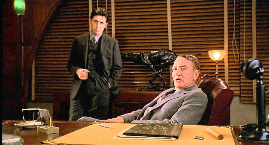 Gabriel Byrne as Tom stands behind Albert Finney as Leo sitting at desk