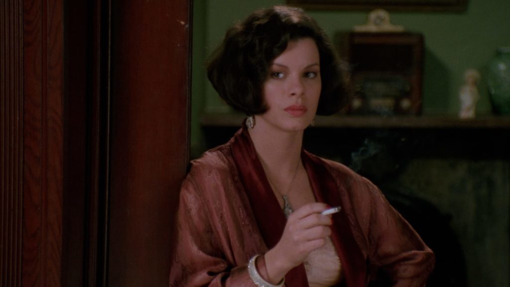 Marcia Gay Harden as Verna dressed in evening wear, smoking a cigarette.