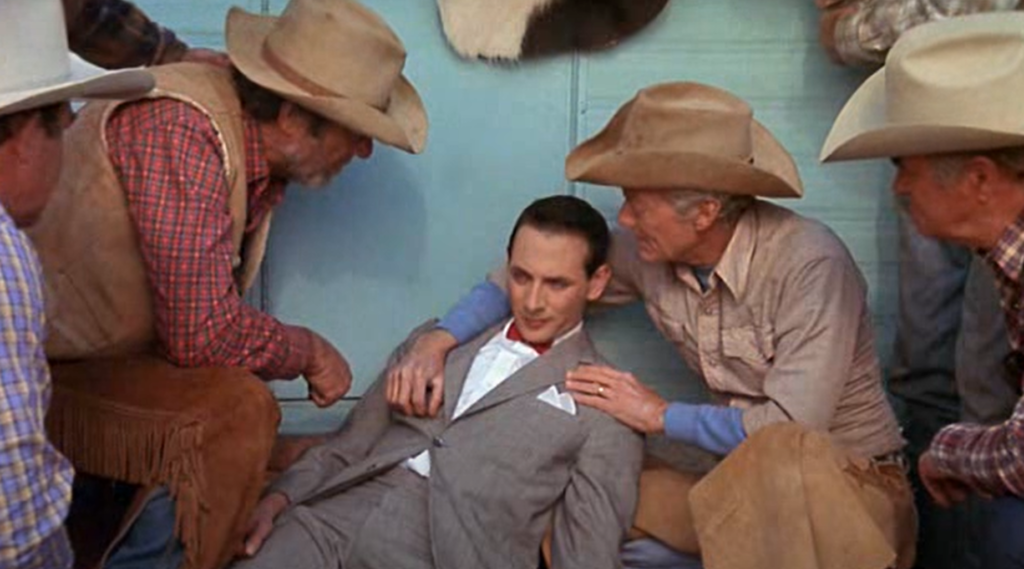 Pee Wee is laying down surrounded by cowboys