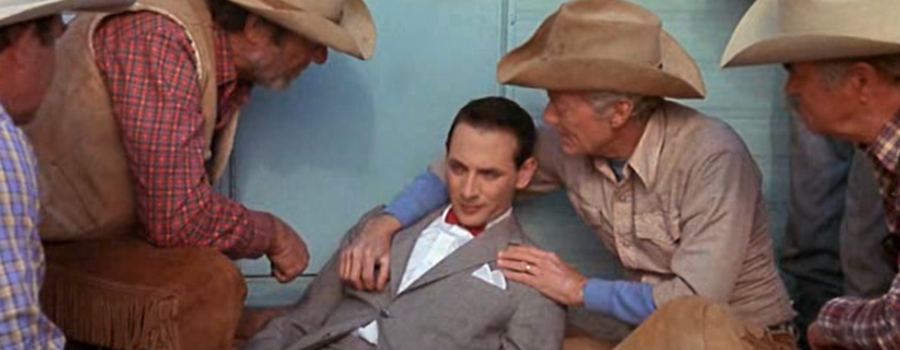 Pee Wee is laying down surrounded by cowboys