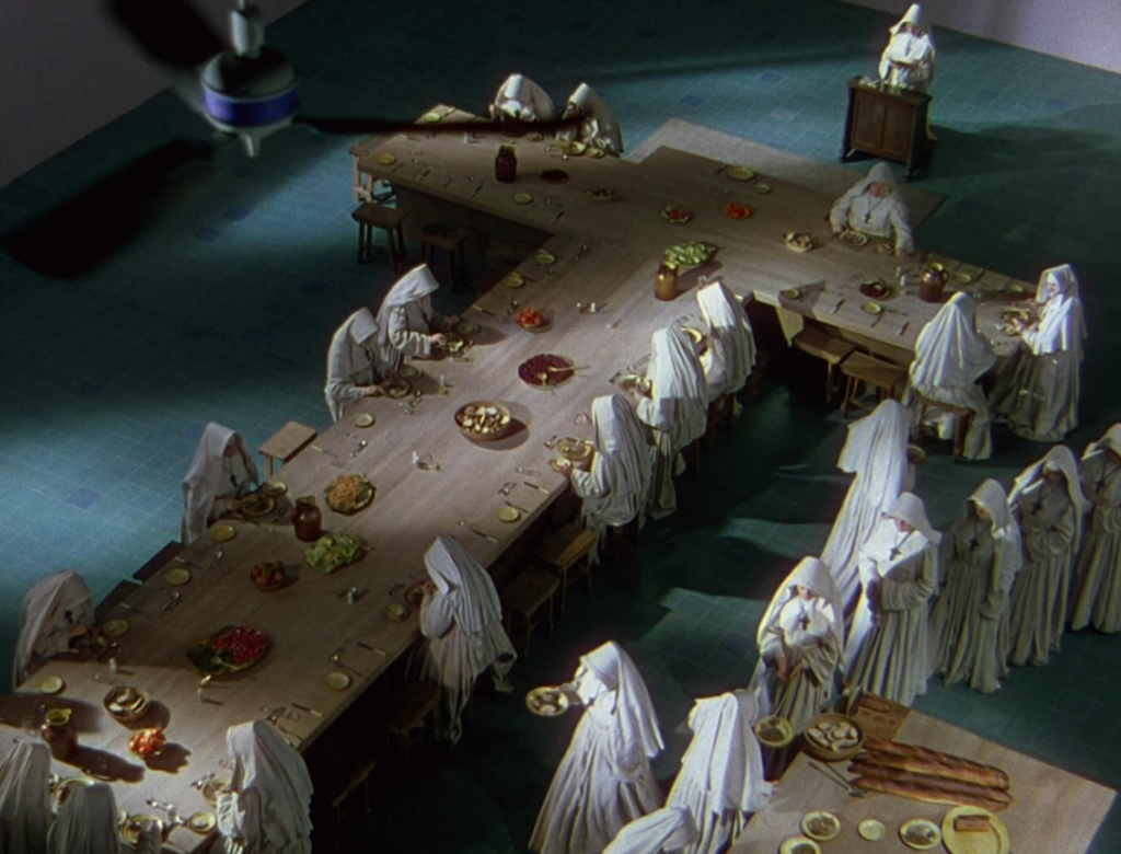 Nuns sit for dinner at a cross-shaped table.