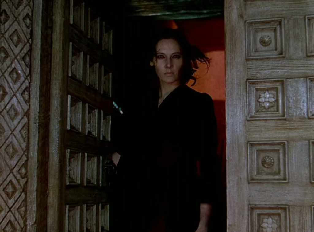 Alt text: Sister Ruth, dressed all in black, glares at the viewer through a darkened doorway.