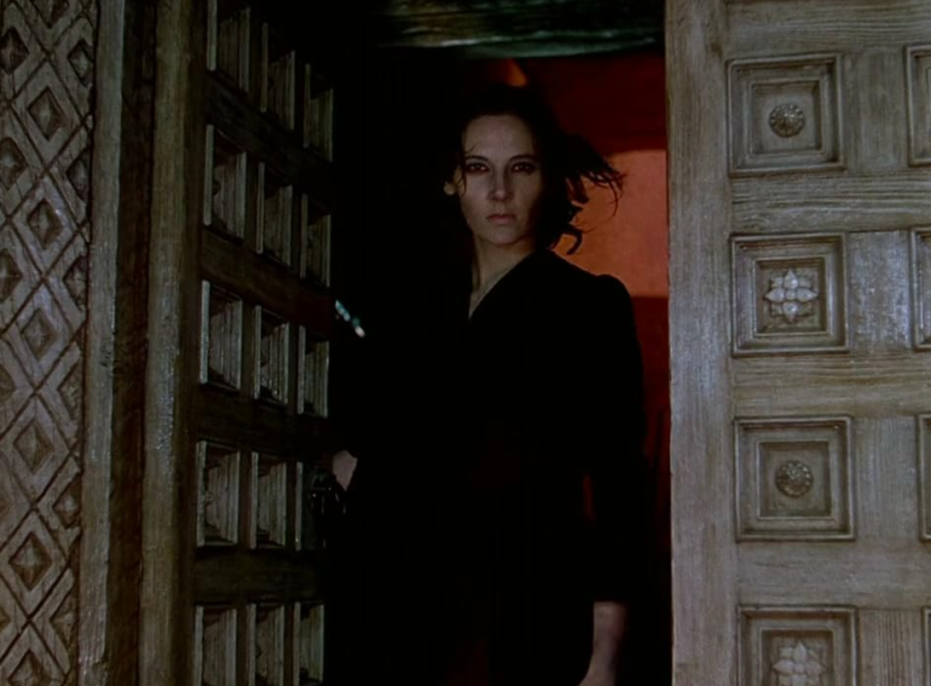 Alt text: Sister Ruth, dressed all in black, glares at the viewer through a darkened doorway. 