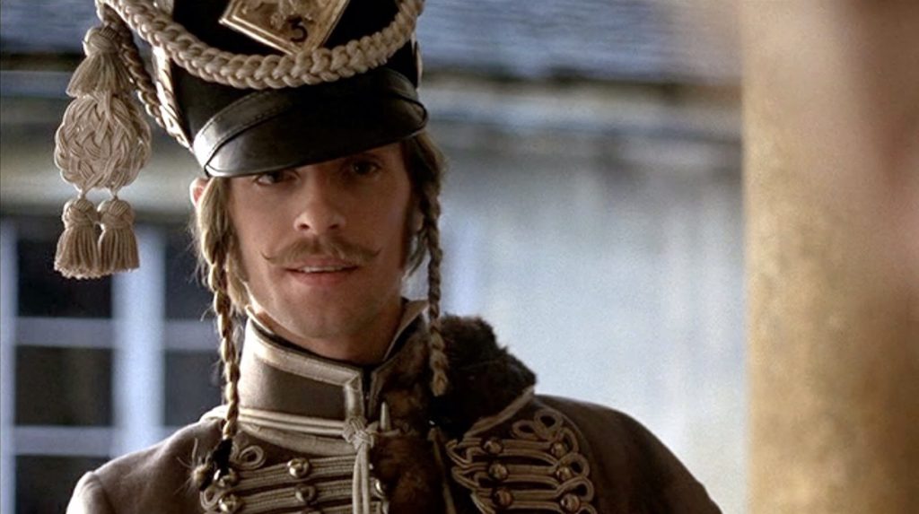 Keith Carradine as d’Hubert smiles slightly.