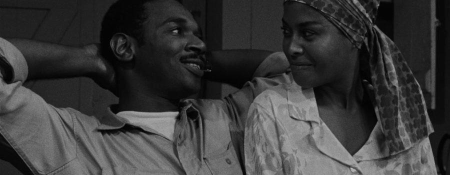 Ivan Dixon as Duff, a young Black man with short hair and a mustache, is sitting with his arms up behind his head, smiling at Abbey Lincoln playin Josie, a Black woman with a patterned scarf around her hair, who reciprocates his smiling glance.