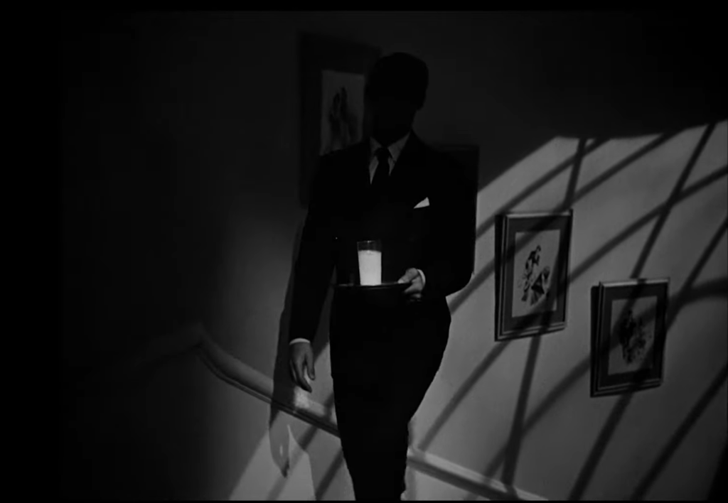 Cary Grant is silhouetted as he ascends the stairs carrying a tray in one hand with a glass of bright white milk on it.