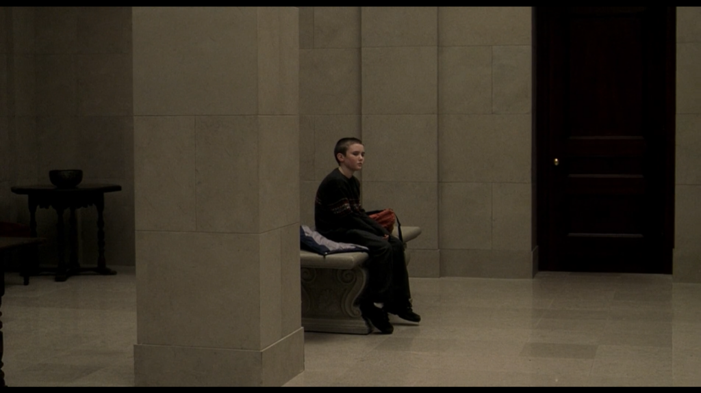 A wide shot of a young boy sitting on a bench in a marble upscale apartment lobby