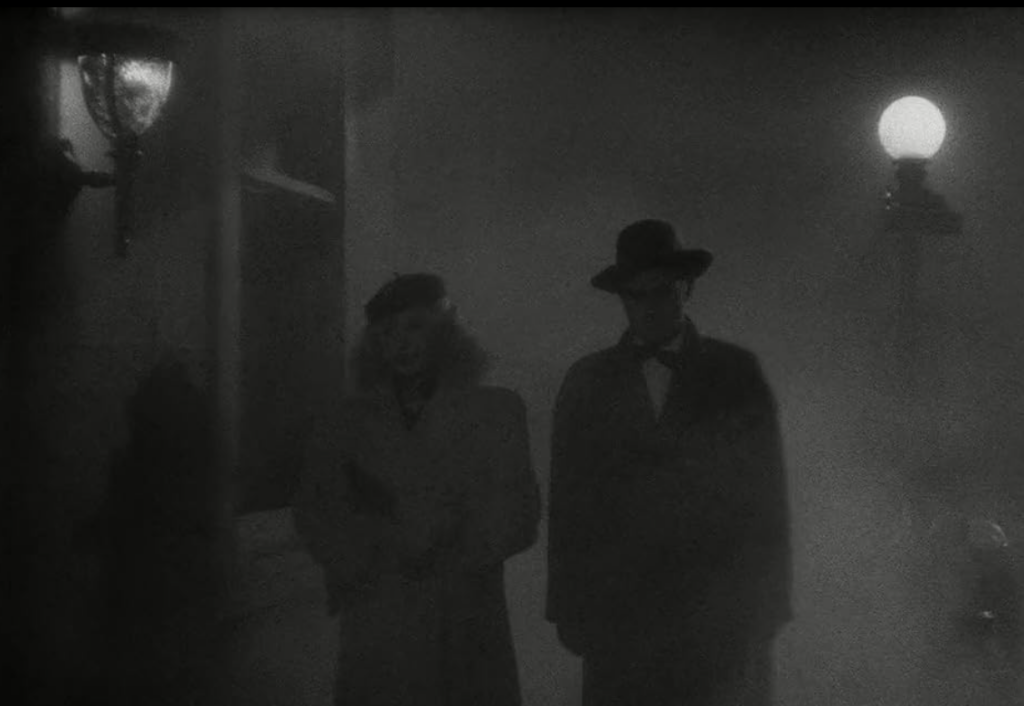 Al and Sue walk through a darkened, foggy city street.