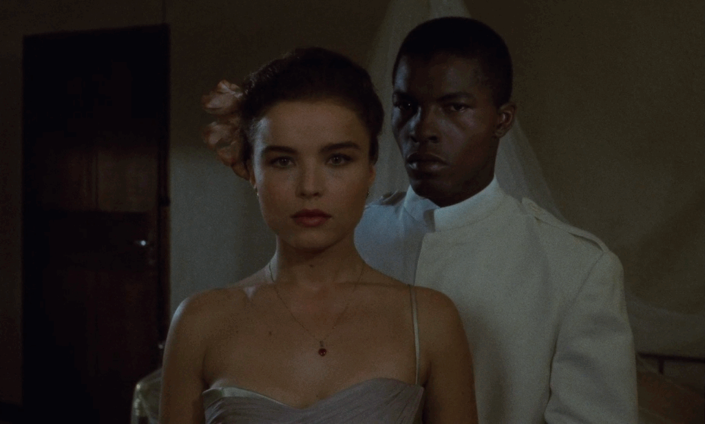 Aimée stands staring in to the camera with Protée over her left shoulder, both in formal dress