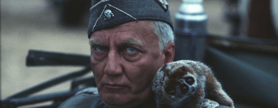 The German commander stares past the camera, a slow loris on his shoulder.
