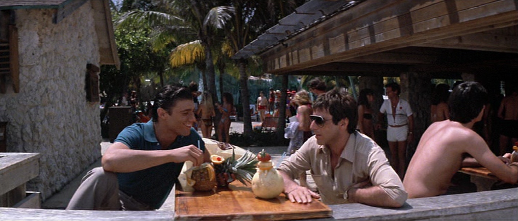 Two men sit at poolside table.