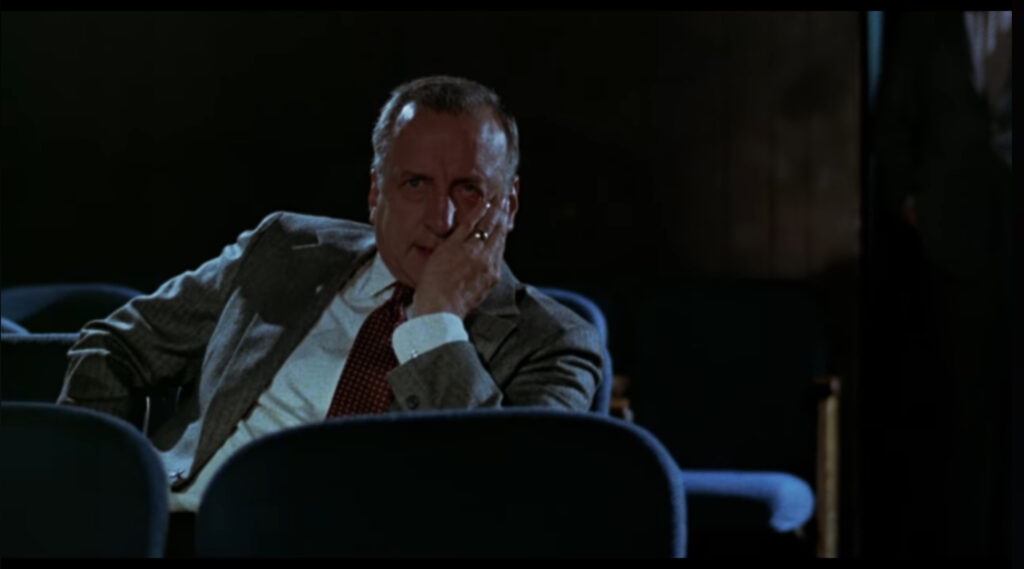 Jake sits in a darkened theater, his head resting on his hand.