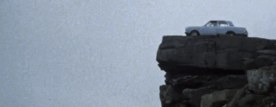 A blue car is parked facing over the edge of a cliff.