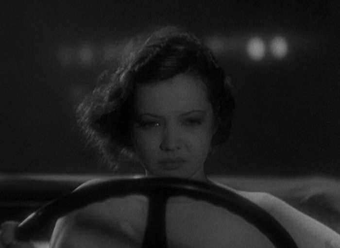 Joan (Sylvia Sidney) driving a car. Her facial expression is a mix of sorrow and disgust.