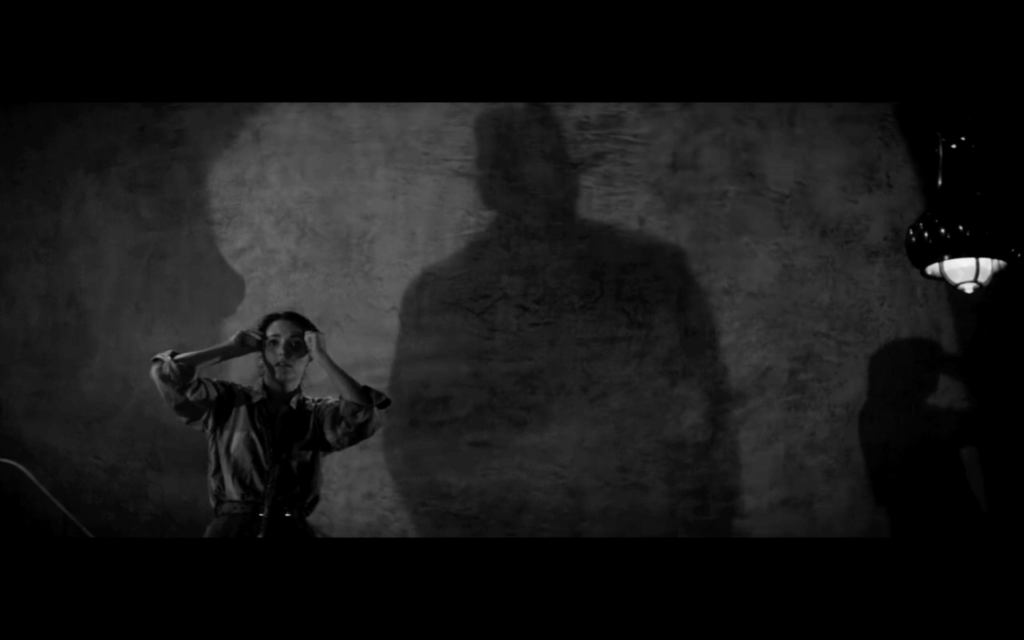 A large shadow of a person in a fedora looms over a woman with dark hair
