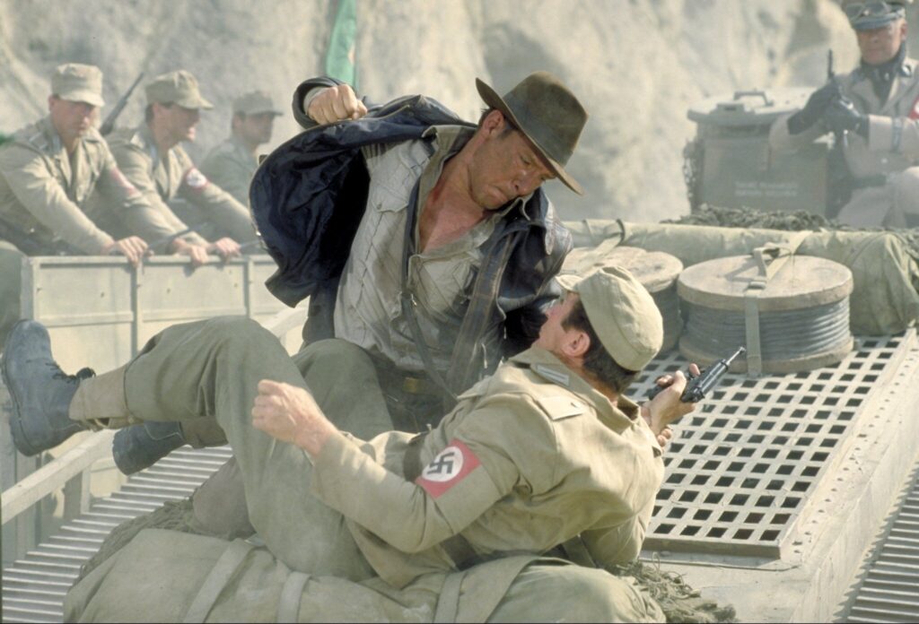 Harrison Ford as Indiana Jones draws back a haymaker on a Nazi soldier on top of a tank