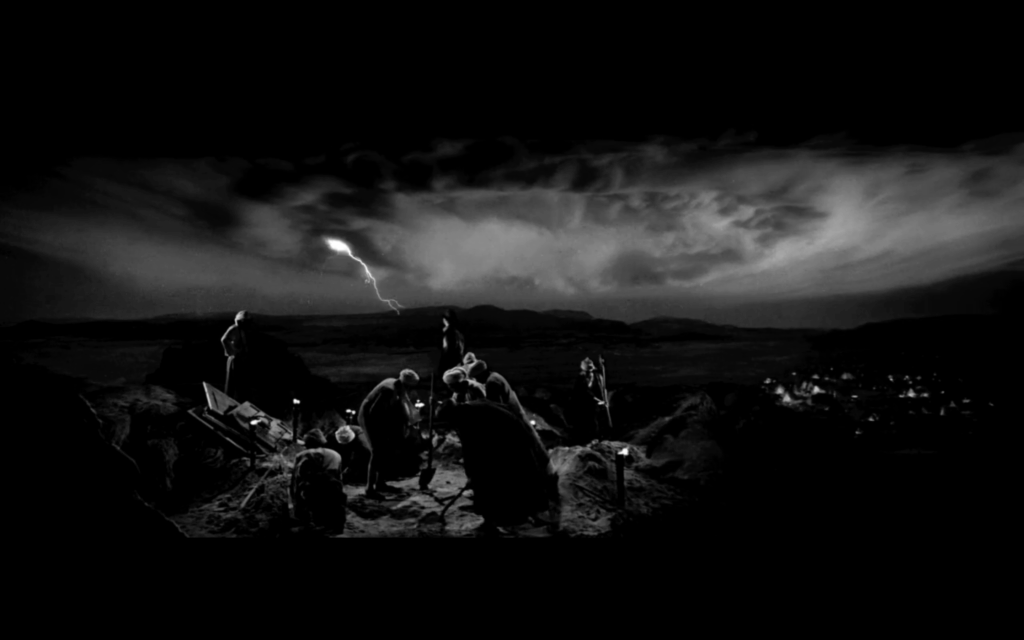 A group of men with shovels dig at the top of a hill at night. Dark clouds are in the sky above them, out of which a bolt of lightning shoots.