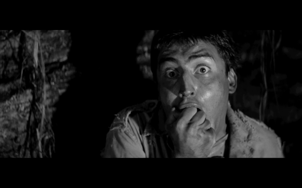 A man with dark hair looks frightened. His eyes are wide, and his fist is held in his mouth