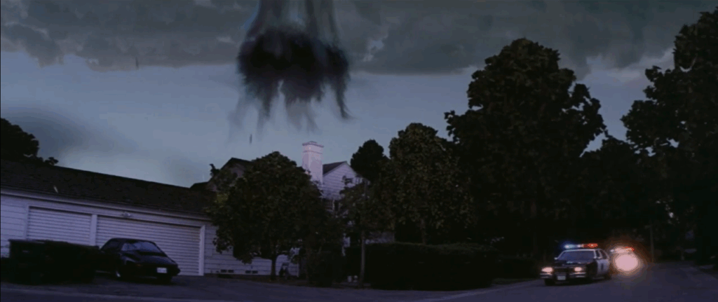 Two police cars pull up to the Darko house at dusk as an unnatural wormhole-like cloud formation forms above their roof.