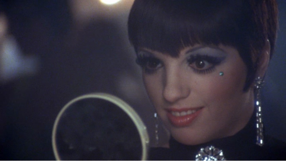 A woman looks into a handheld mirror.