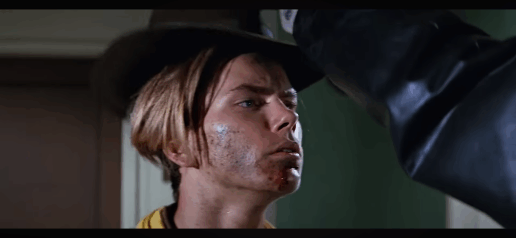 ALT TEXT: River Phoenix as a young Indiana Jones dons the iconic hat that defines the character’s appearance.