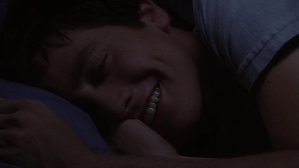 a close up of Donnie Darko, a teenager, in his bed, smiling.