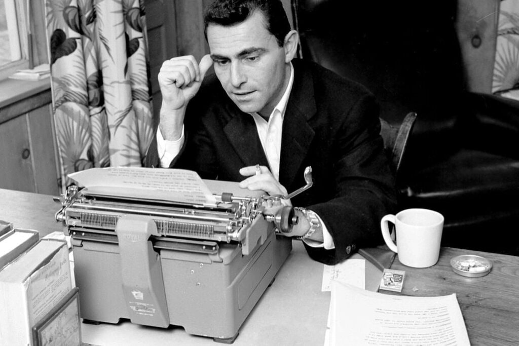 Rod Serling, sitting at his desk with a cigarette in his hand, reading back over something he has just written, the paper still in his typewriter.