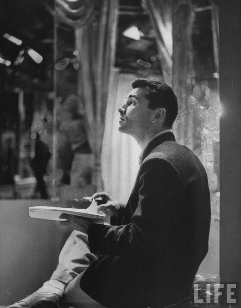 Life Magazine picture of Rod Serling behind the scenes, holding a script and a cigarette. He’s in profile. His leg is crossed, he is in profile, and is looking slightly up.