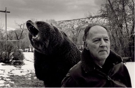 a black and white image of a man in a fur jacket with a bear behind him.