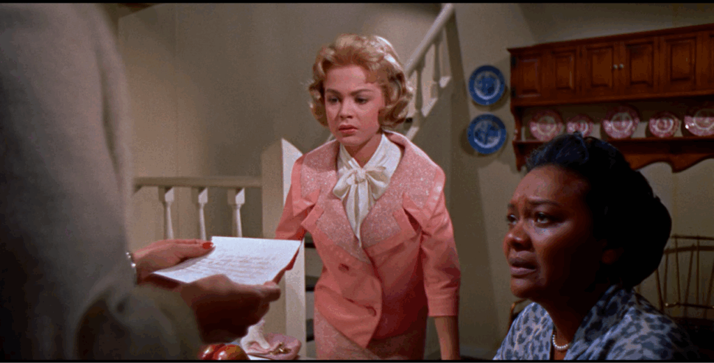 Susie (Sandra Dee) and Annie (Juanita Moore) sit in a kitchen and react to Lora (Lana Turner) reading a letter. Susie has a worried expression and Annie cries.