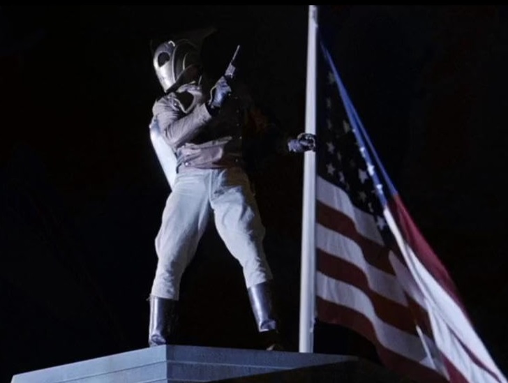 The Rocketeer brandishes a gun in front of an American flag