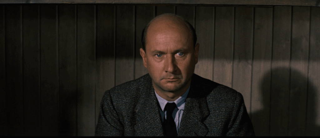Colin Blythe (Donald Pleasance) sits on his bed, looking into the distance with a pained expression