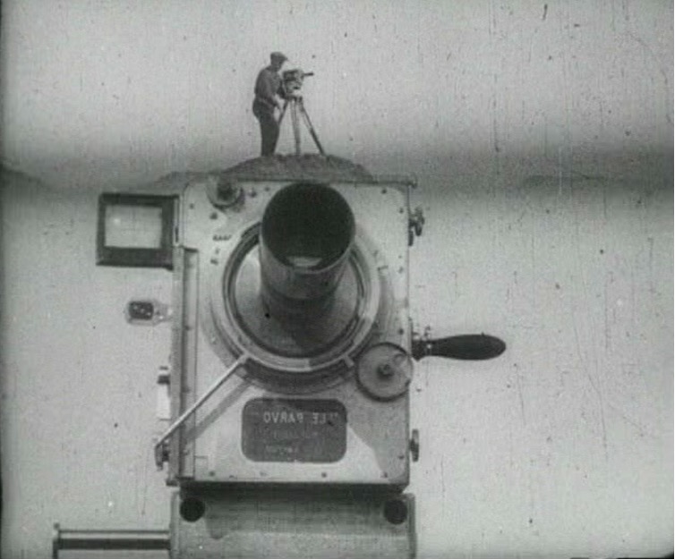 A man stands atop a giant camera.