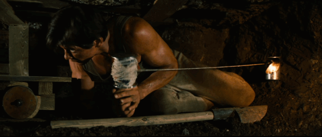 Shot of Charles Bronson with a shovel, lamp, and spool of twine in a claustrophobic tunnel