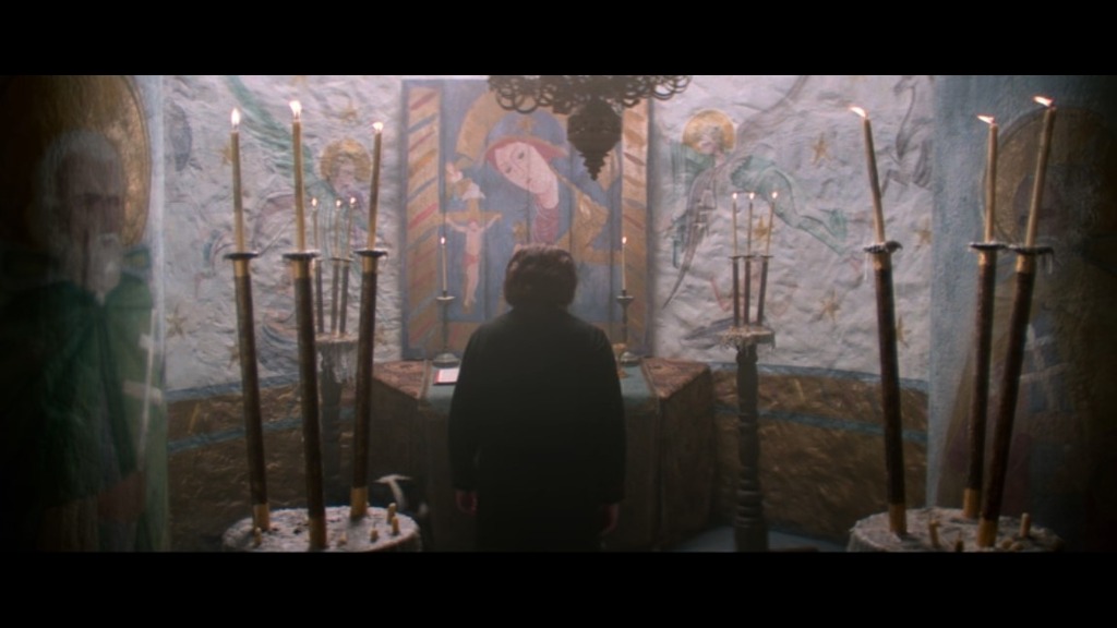 a priest stands with his back facing the audience in a vividly painted church